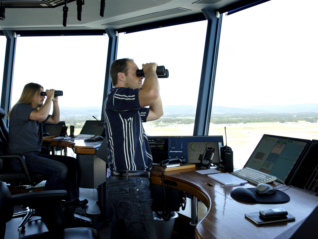 Flygeledere i en flykontrolltårn overvåker flytrafikken ved hjelp av kikkert og dataskjermer.
