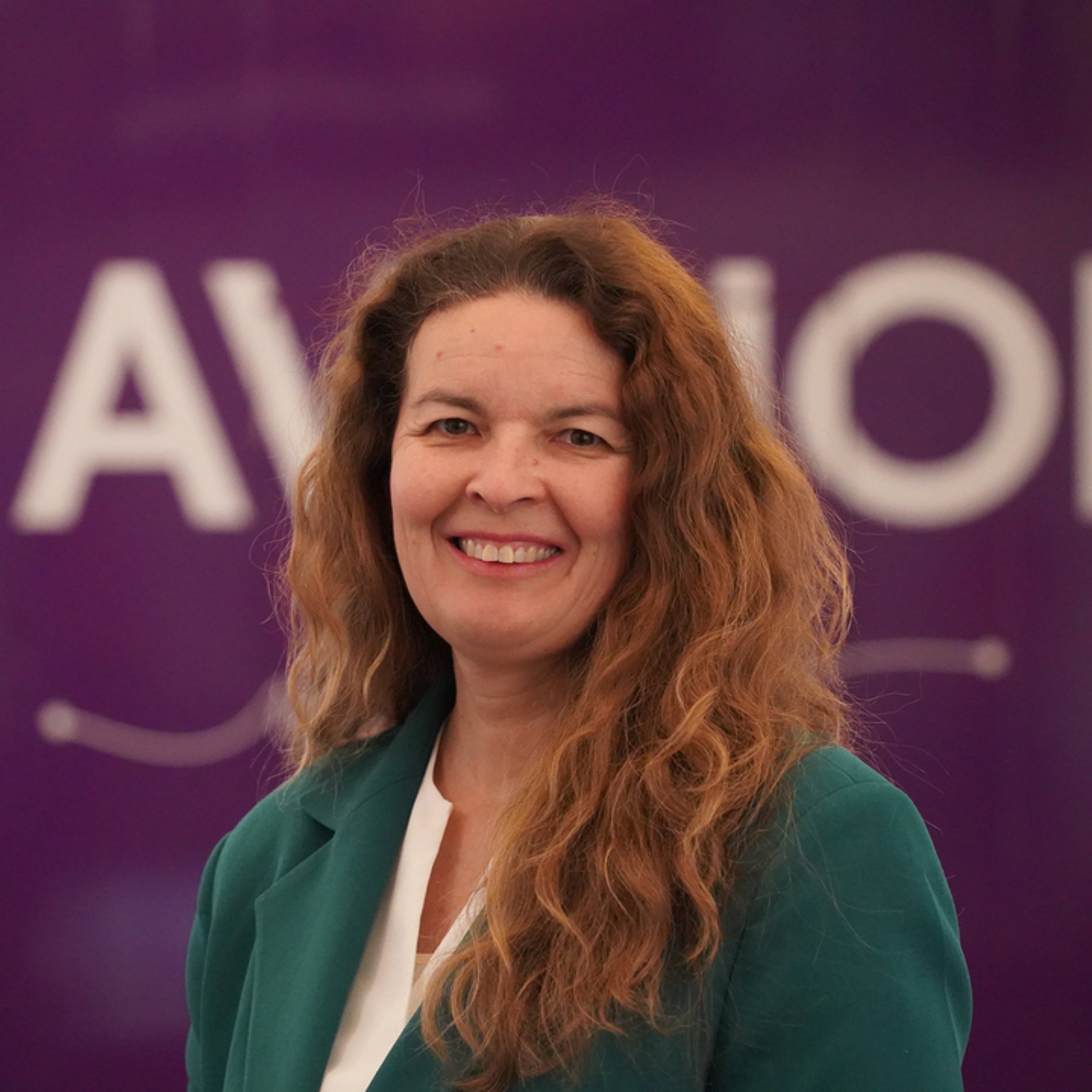 Kvinne i grønn jakke foran en lilla bakgrunn med teksten "AVINOR".