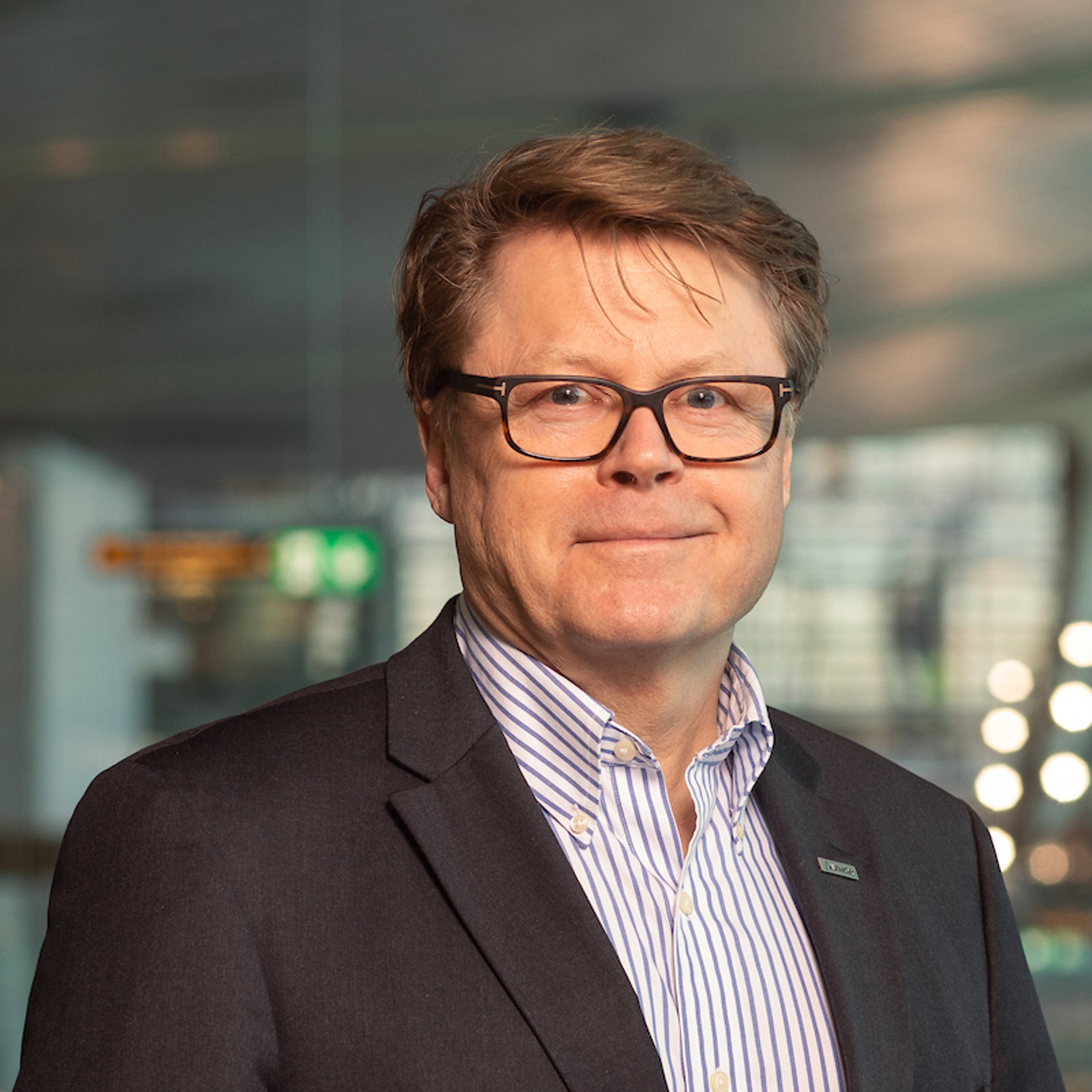 Person i dressjakke og briller i moderne kontorinteriør.