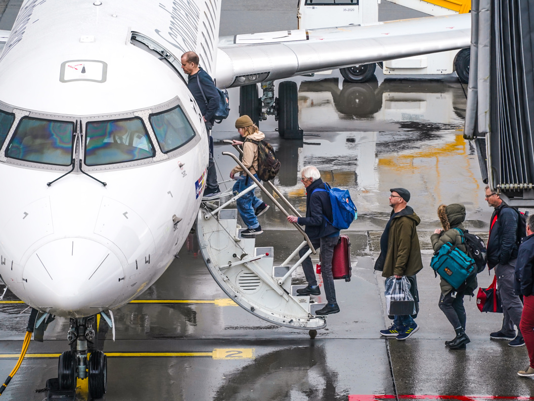 Passasjerer går om bord i et fly på en regntung dag på flyplassen.