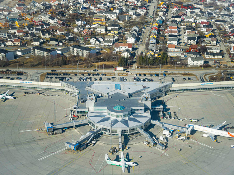 Flyfoto av Bodø lufthavn med fly på bakken, terminalbygning og omkringliggende nabolag i Bodø, Norge.