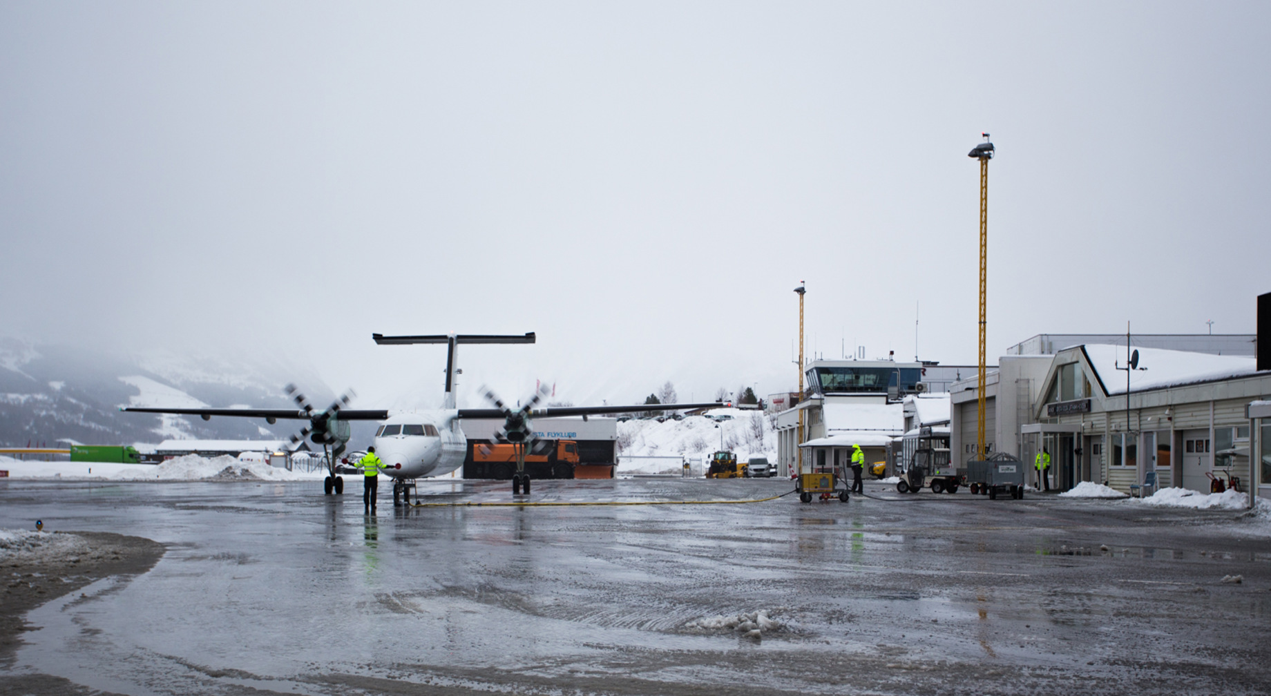 Flyplass med fly på rullebanen om vinteren, omgitt av snødekte fjell.