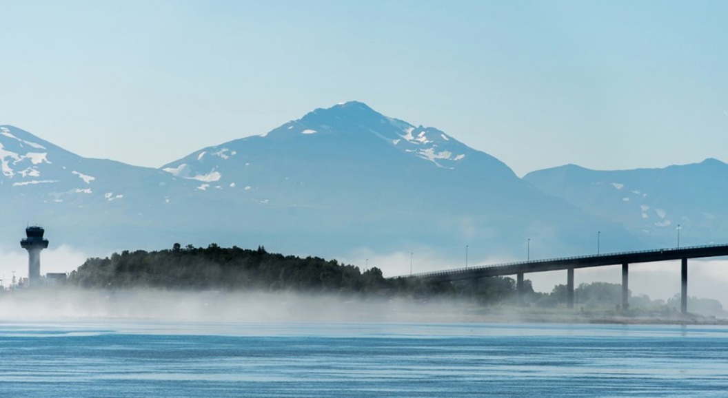 Bro over vann med fjell i bakgrunnen ved Ålesund, Norge, innhyllet i tåke.