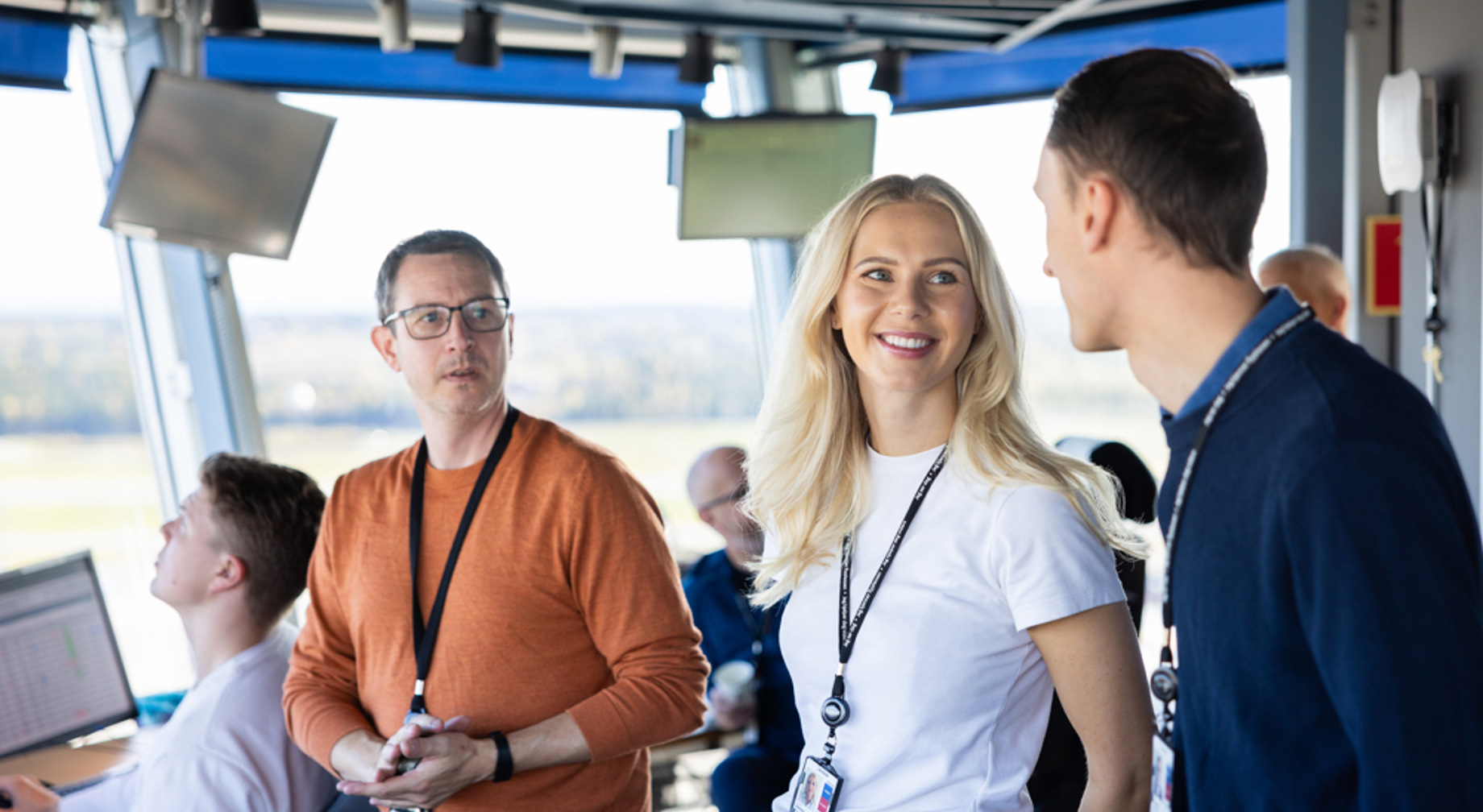 Kontrolltårn på flyplass med flygeledere i samtale, skjermer i bakgrunnen.