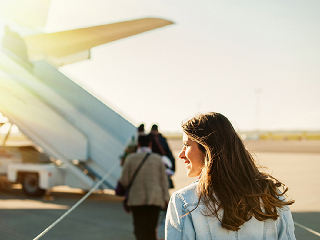 Kvinne går mot flytrapp i solfylt vær på flyplass.
