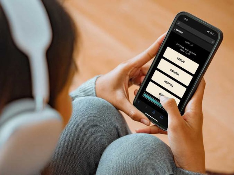 Person med hodetelefoner holder en smarttelefon som viser en quiz-app med spørsmål om planeter.
